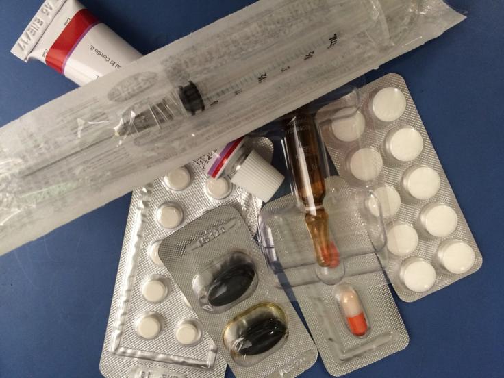Foto mit verschiedenen Tabletten in Verpackung, einer Ampullem, einer Salbe und einer noch eingepackten Spritze.